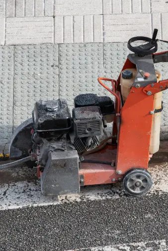 a mall orange machine positioned on the roadside, surrounded by grass and pavement, indicating a work zone or maintenance area