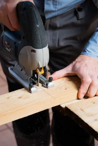 a man skillfully operates a jigsaw to cut a piece of wood in a workshop setting