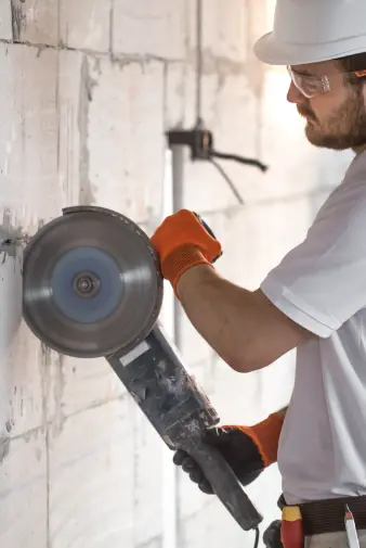 a man wearing a hard hat and safety glasses operates a circular saw, demonstrating safety in construction work.